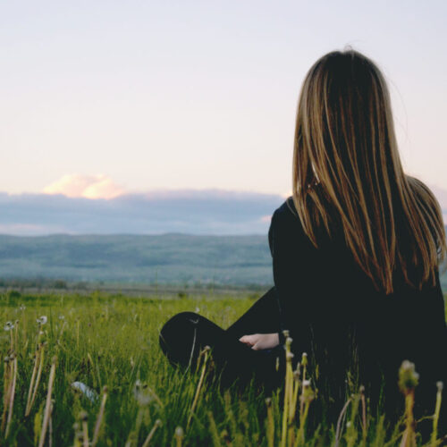 Woman sitting alone in grass looking off into the distance