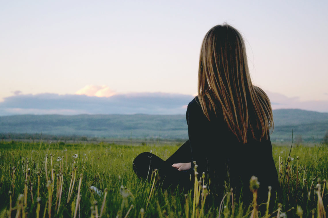 Woman sitting alone in grass looking off into the distance